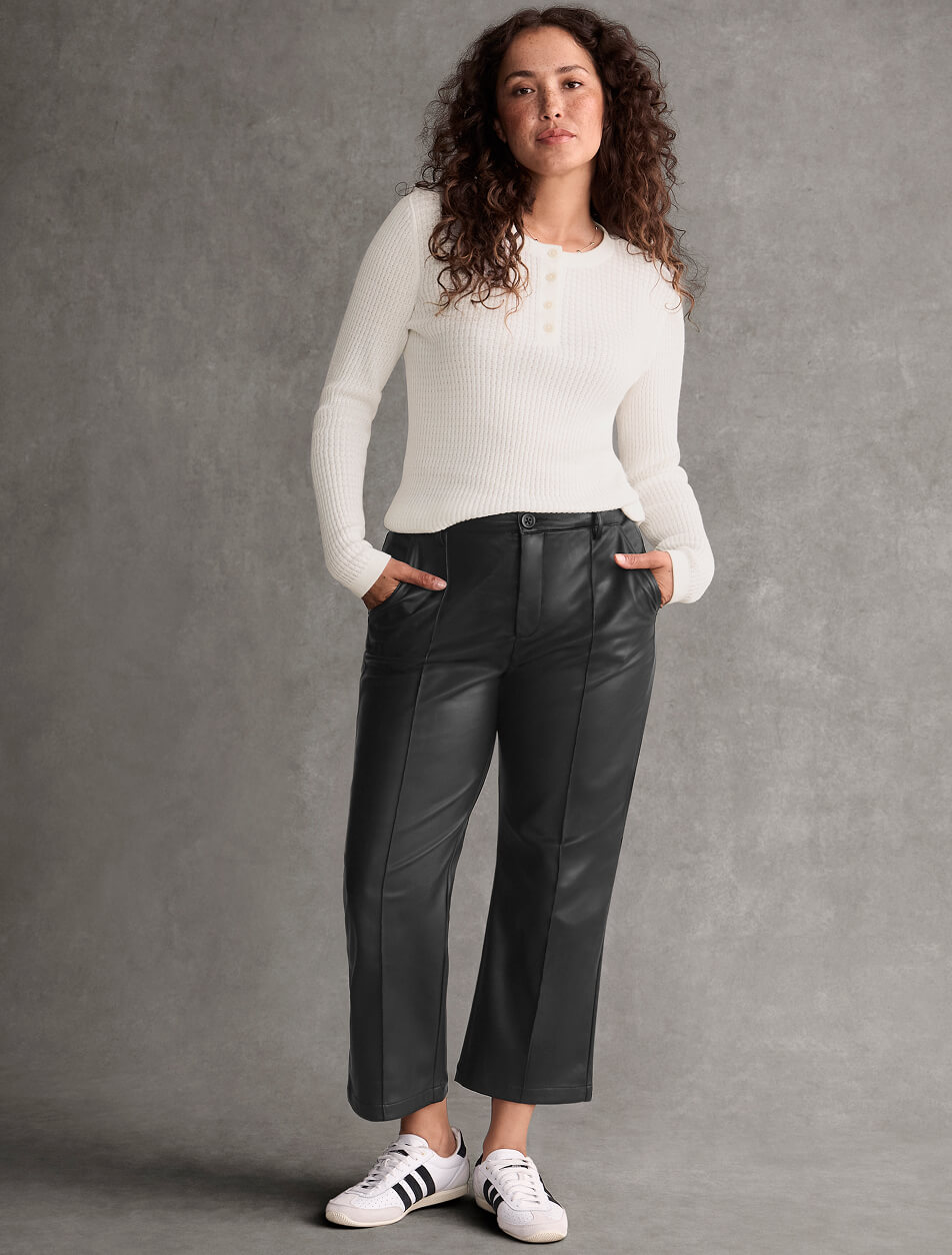 A female model wearing a white long-sleeve top with black pleather pants