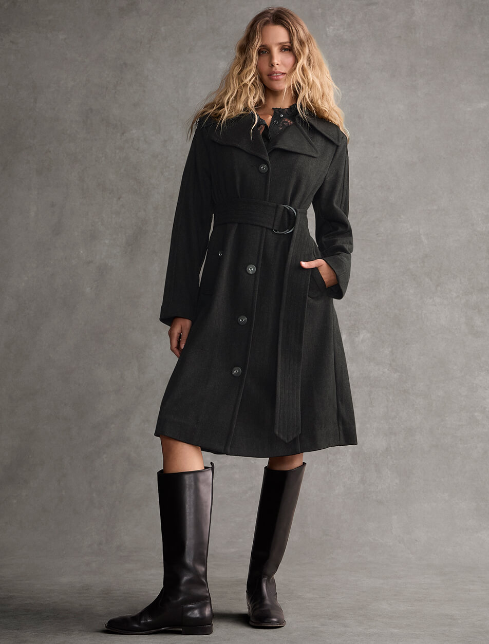A female model wearing a long black coat with black leather boots